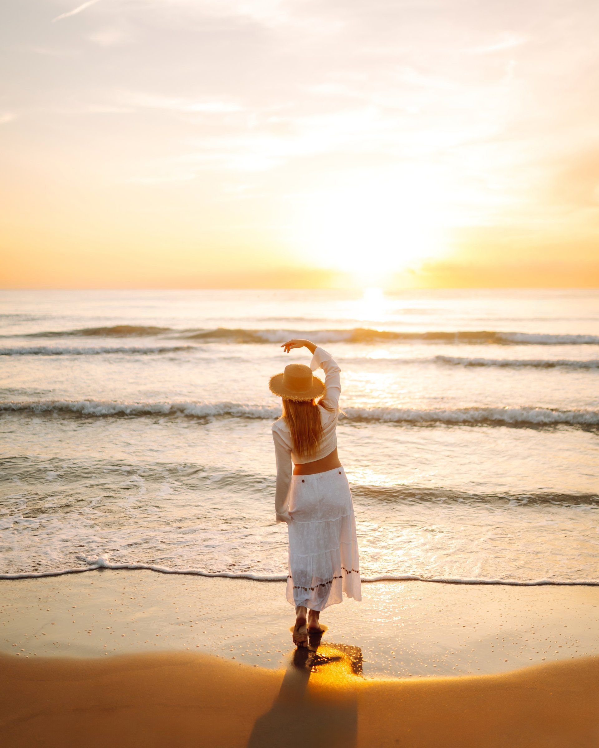 Sunset over the sea, with a woman walking along the beach